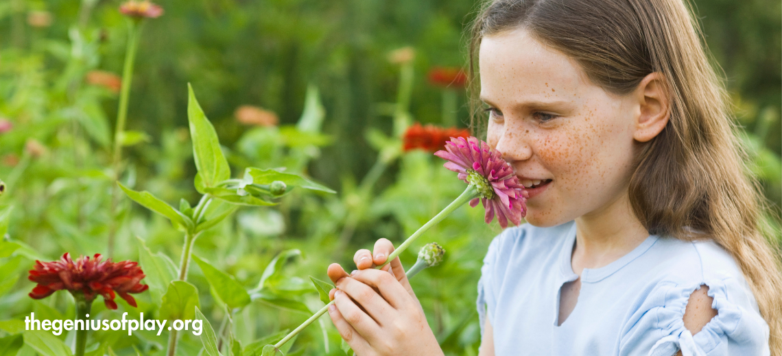 young freckled face girl smelling flowers in an outdoor garden